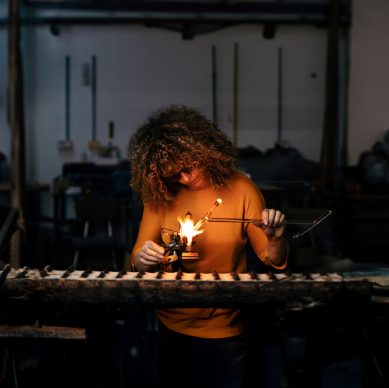 Front view of woman lampworker working with glass tubes with the torch flame. Concept of glassblowing, lampworking.